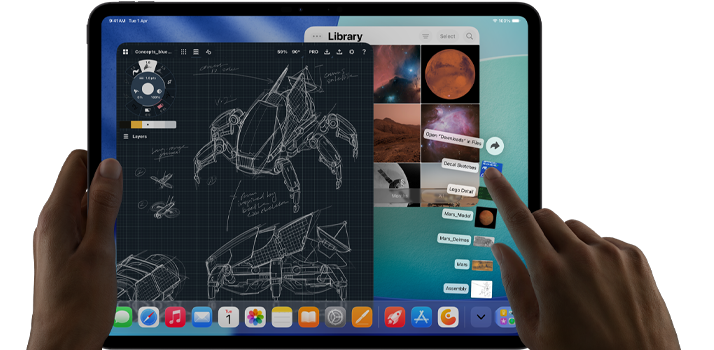 iPad Pro, space black colour, left hand holding device, right hand pointing gesturing to manipulate multiple open app windows, a drawing app with sketches of mechanical designs, photos library of planets and space images, downloads folder files fanned out