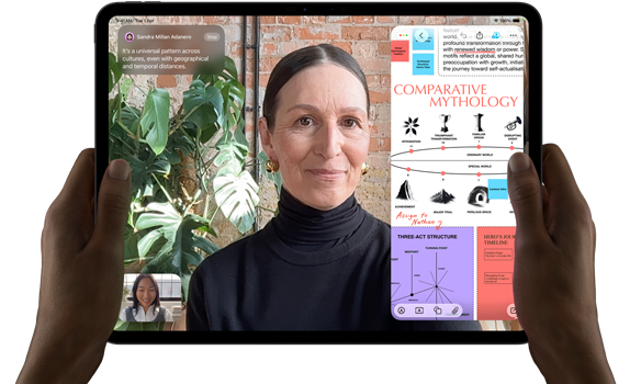 iPad Pro, front exterior, landscape orientation, space black colour, rounded corners, black display bezel, hands holding left and right sides, display showing a FaceTime conversation being live translated, and an educational app showing a presentation of “Comparative Mythology” with text, diagrams and handwritten notes